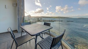 A balcony with a table and chairs overlooking a coastal view.