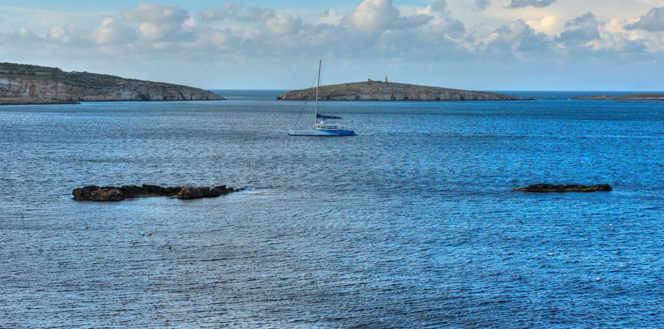 Ruhiges Meer mit Segelboot und Felsen.