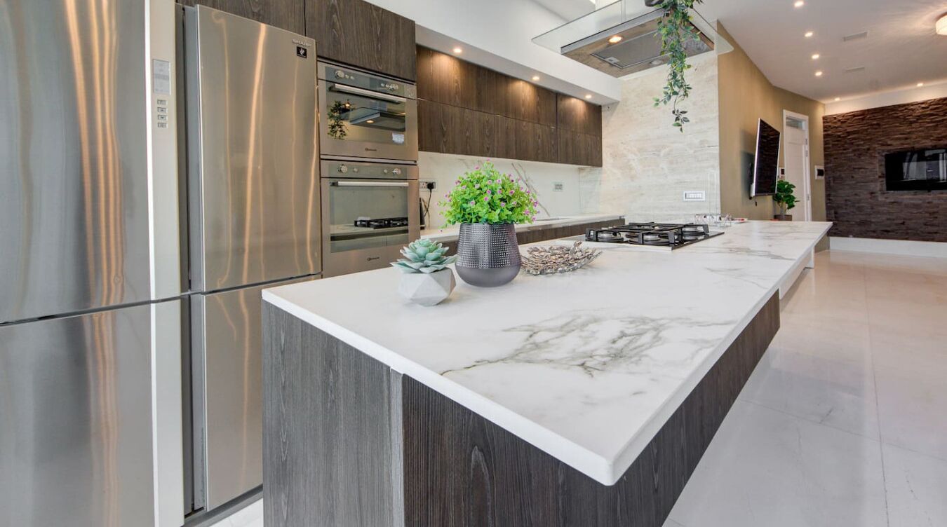 A modern kitchen with a large island, stainless steel appliances, and a stone accent wall.
