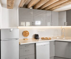 A modern kitchen with grey cabinets, a built-in dishwasher, and a wooden ceiling beam. - 1596 Nazareth (Paris)