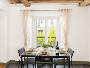 Une table à manger dressée pour quatre personnes, avec des chaises, une bouteille de vin et une fenêtre avec des rideaux.