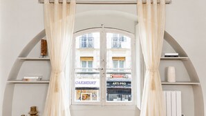 A room with a large arched window, white curtains, and wooden beams on the ceiling. - 1596 Nazareth (Paris)