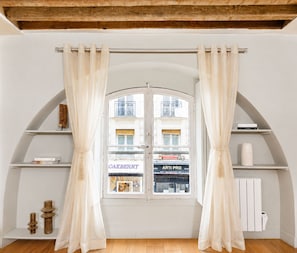 Une pièce dotée d’une grande fenêtre en arc de cercle, de rideaux blancs et de poutres en bois au plafond.