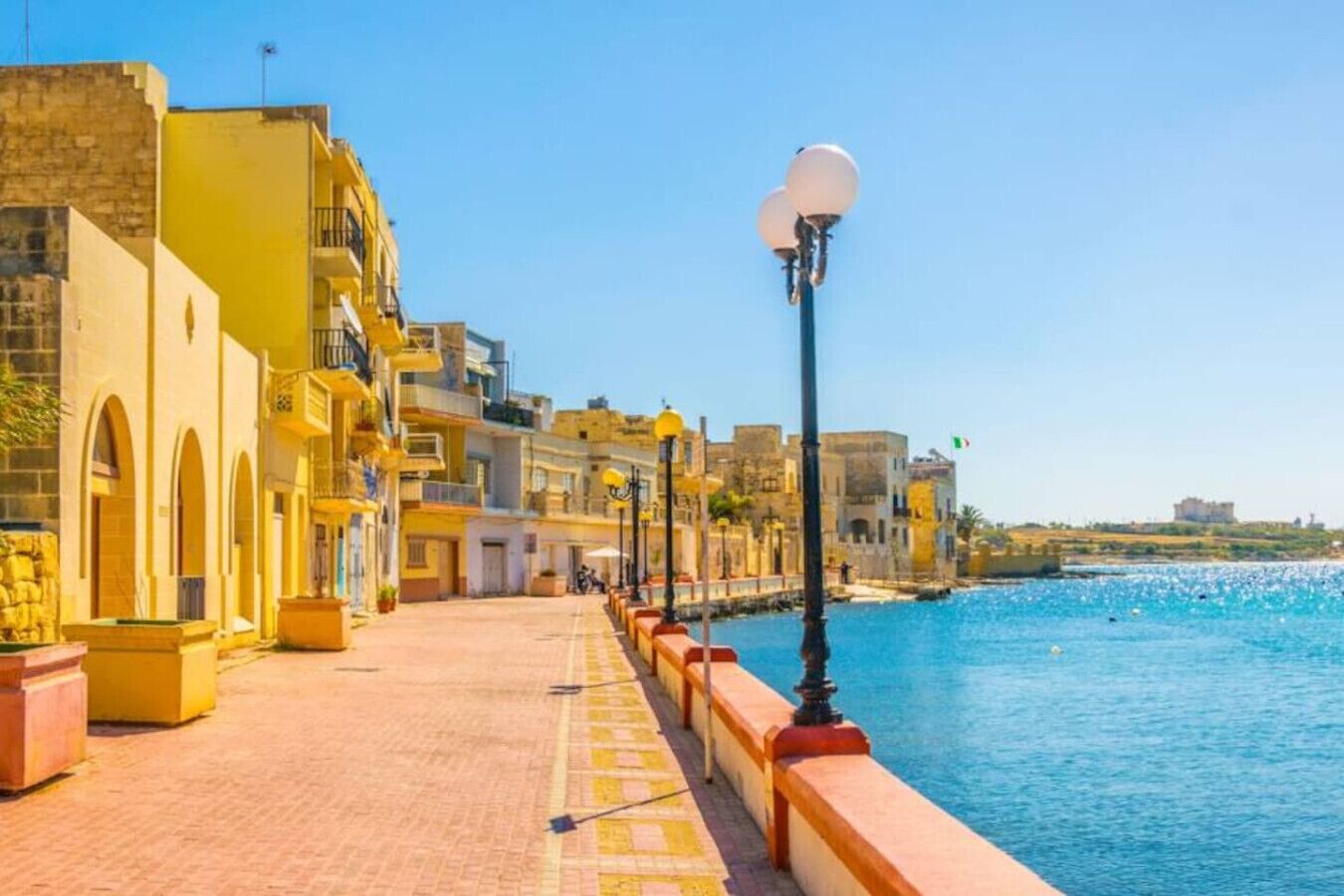Un paseo marítimo con edificios a un lado y un mar azul y despejado al otro.