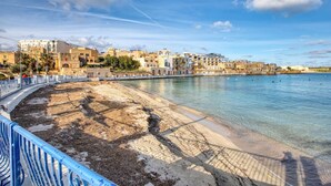 Un pueblo costero con una playa de arena, una barandilla azul y edificios al fondo.