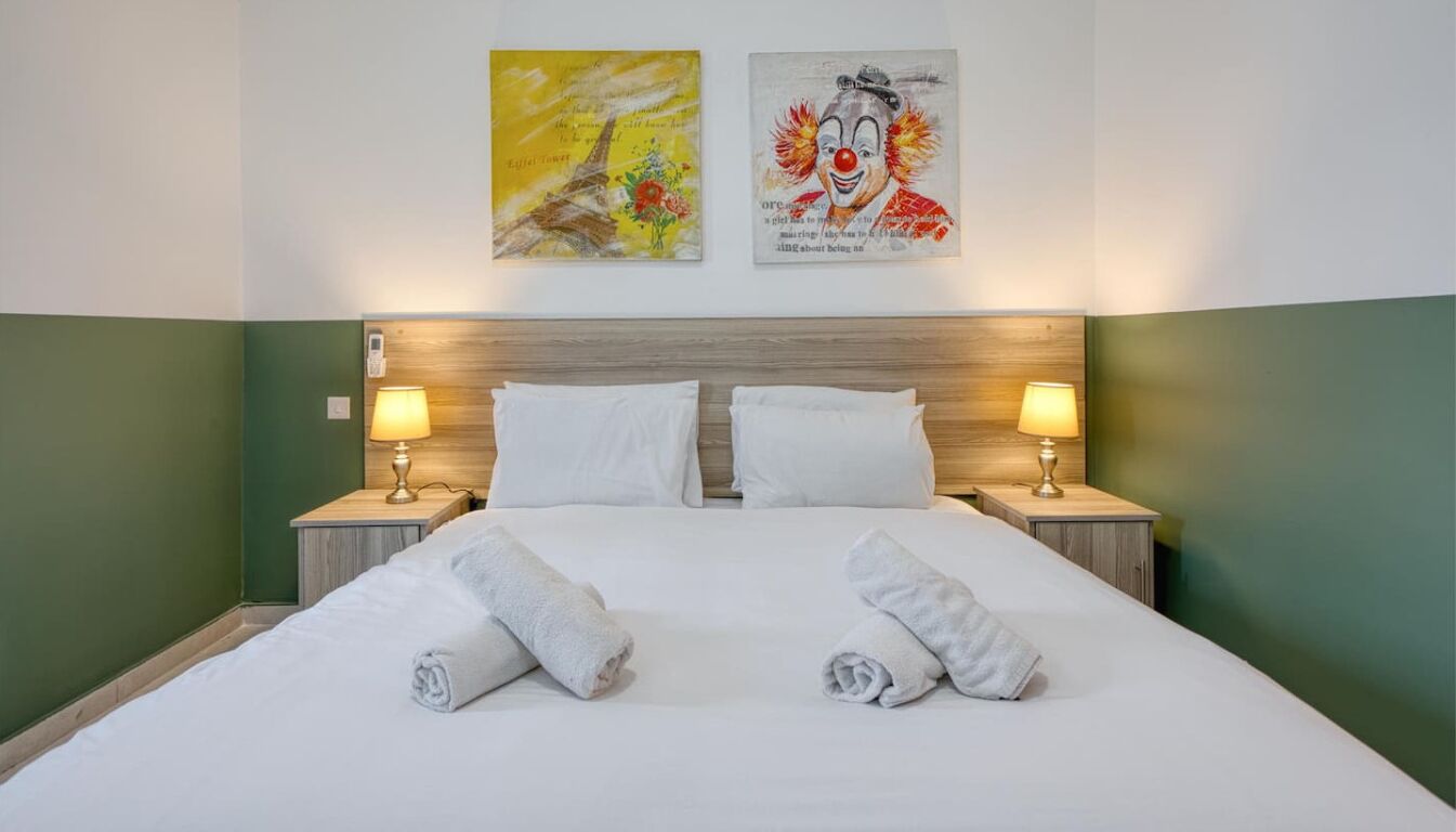 Een hotelkamer met een groot bed, twee nachtkastjes met lampen en twee kunstwerken aan de muur.