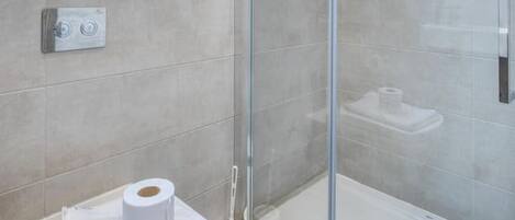 A modern bathroom with a glass shower enclosure, a toilet with a towel and toilet paper, and a window above the toilet.