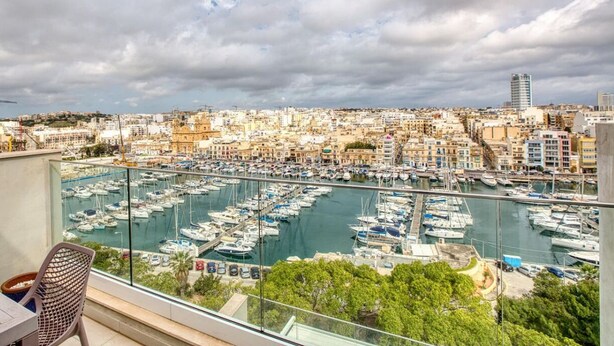 A balcony with a view of a marina filled with boats, a cityscape in the background, and a construction crane.