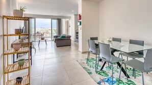 A modern living room with a glass dining table, grey chairs, and a view of the city.