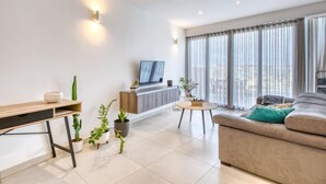 A modern living room with a sofa, a coffee table, a TV, and potted plants.