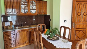 A kitchen with wooden cabinets, a sink, and a dining table with chairs. - Apartments Meleqi (Ksamil)