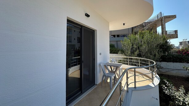 A balcony with a glass door, a metal railing, and a view of a building in the background. - Apartments Meleqi (Ksamil)