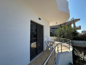 A balcony with a glass door, a metal railing, and a view of a building in the background. - Apartments Meleqi (Ksamil)