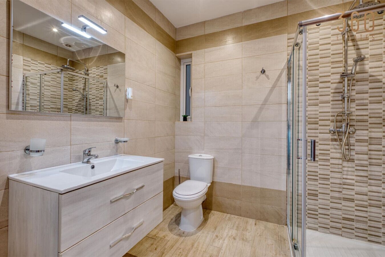 A modern bathroom with a large mirror, a sink, a toilet, and a glass-enclosed shower area.
