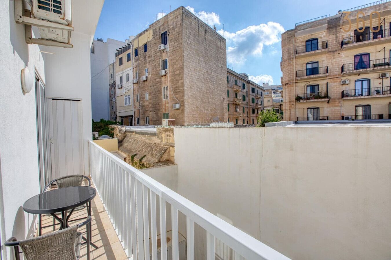 A balcony with a table and chairs, overlooking a row of multi-story buildings with balconies.