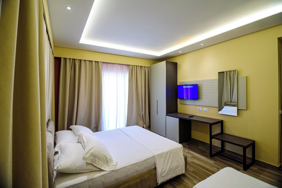 Quarto de hotel com cama, escrivaninha, televisão e espelho.