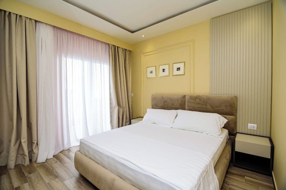 Ett hotellrum med en stor säng, beige gardiner och ett trägolv.