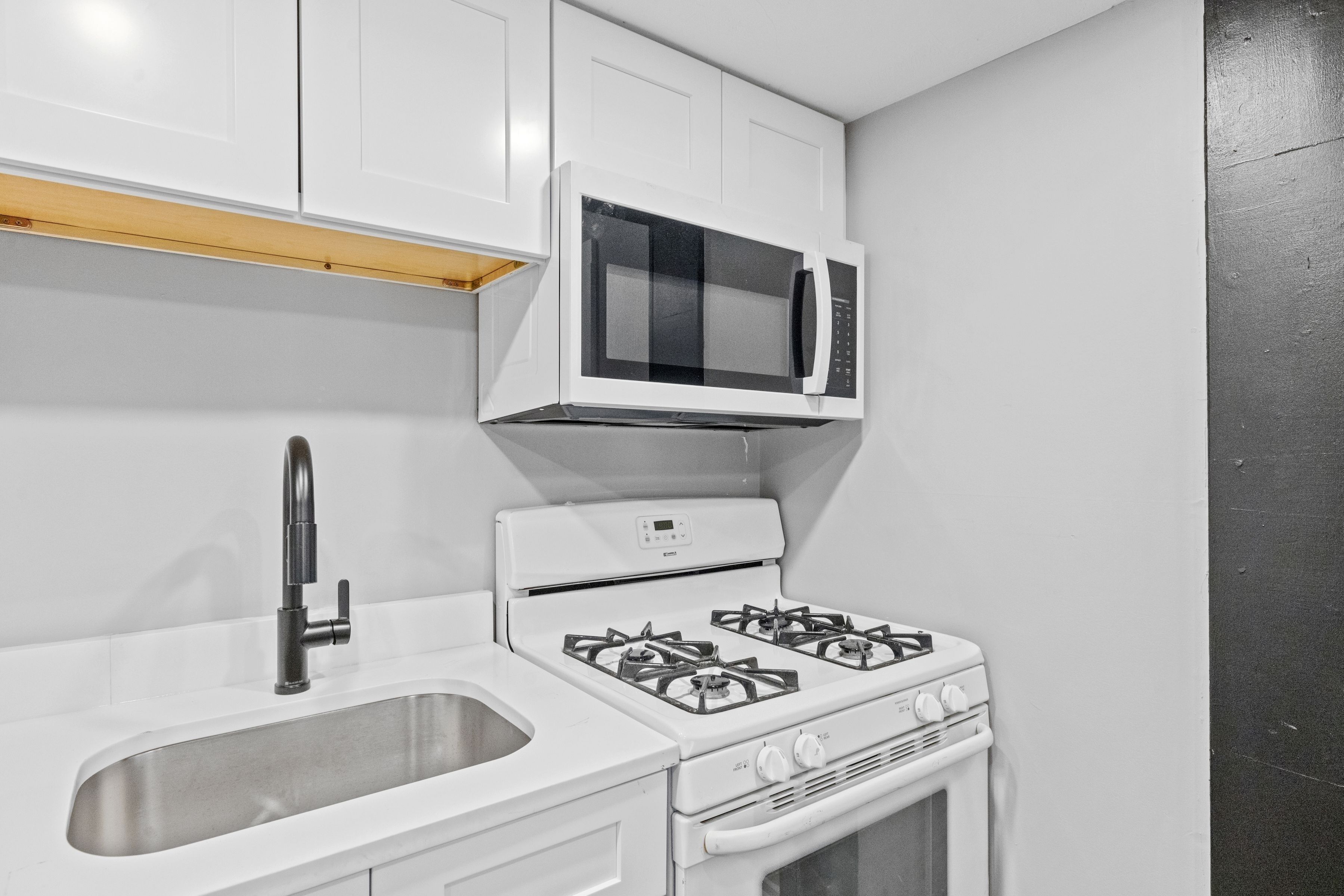 A kitchen with white cabinets, a stainless steel sink, a microwave, and a gas stove.
