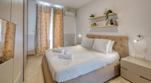 A hotel room with a large bed, a bedside table, a wardrobe, and a wall-mounted shelf with plants. - Sunlit Sliema 2BR Penthouse, Steps to Seafront! (Sliema)