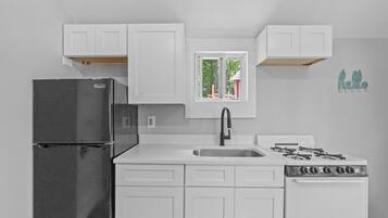 A kitchen with white cabinets, a black refrigerator, a stove, and a window with a view of trees.