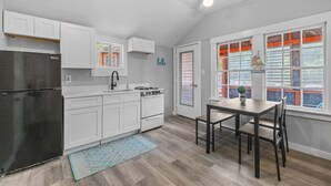 A modern kitchen with white cabinets, a black refrigerator, a stove, and a dining area with a table and chairs.