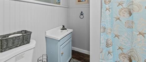Un bagno con un mobile lavabo bianco, uno specchio sopra il lavello, un soffitto in legno e una tenda da doccia con motivo a conchiglia.