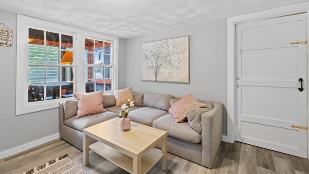 Ein Wohnzimmer mit einem beigen Sofa, einem Holztisch und einem großen Fenster mit Blick auf einen Balkon.
