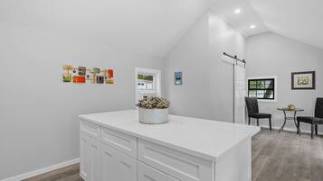 Una cocina moderna con armarios blancos, una isla central y un pequeño comedor con dos sillas y una mesa.