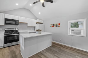 A kitchen with white cabinets, a black microwave, a stove, and a ceiling fan.