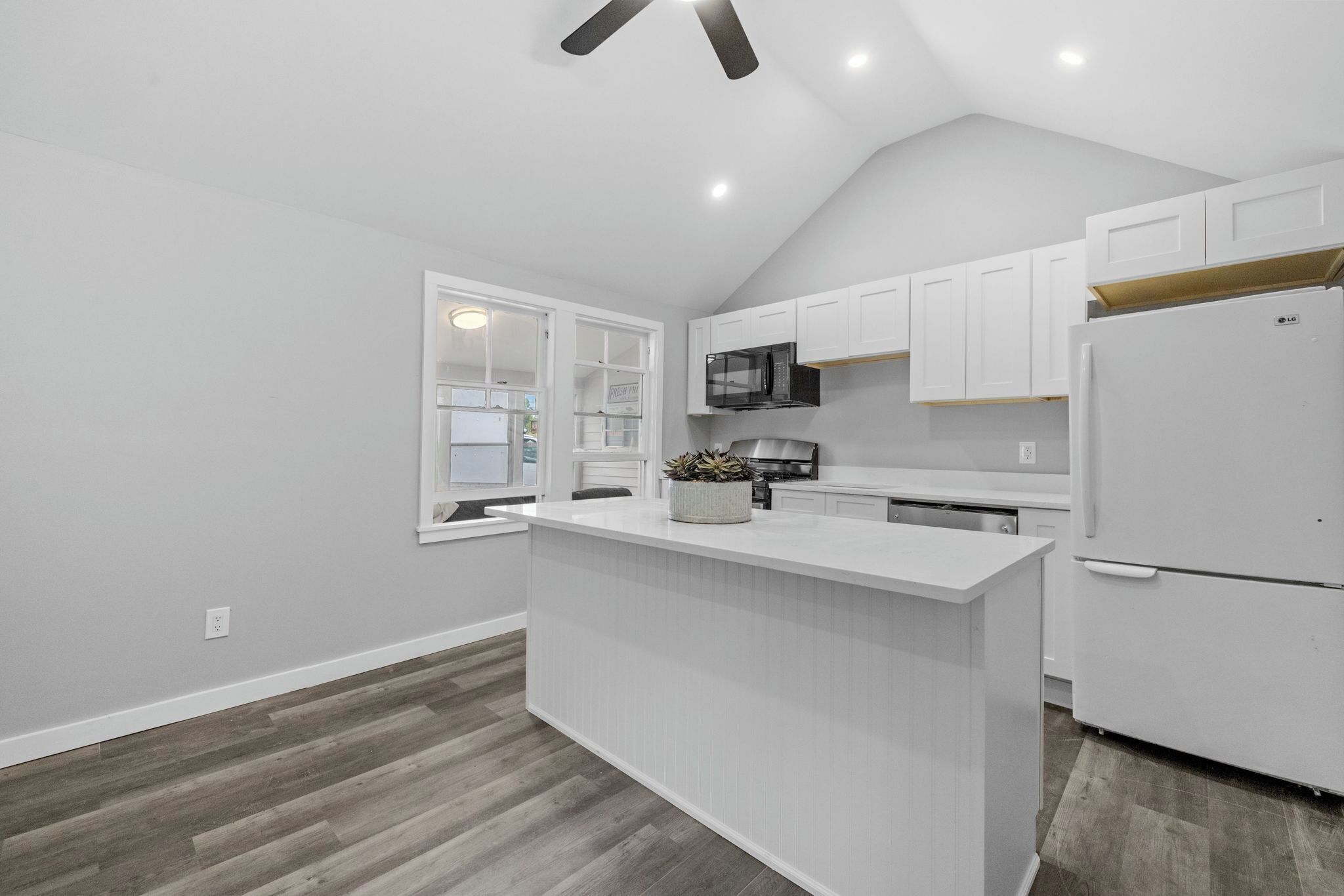 Una cocina moderna con armarios blancos, una isla central, un microondas y un refrigerador.