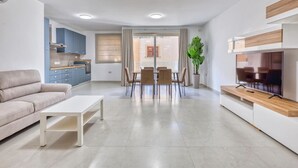 Un salon moderne avec un canapé, une table basse, un coin repas avec des chaises, un téléviseur et une cuisine en arrière-plan.