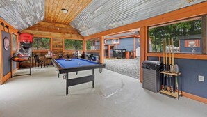 Zona recreativa interior con mesa de billar, sillas y un soporte para equipo deportivo.