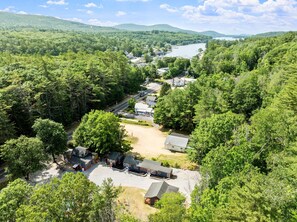A residential area with houses and a road, surrounded by dense forest and hills.
