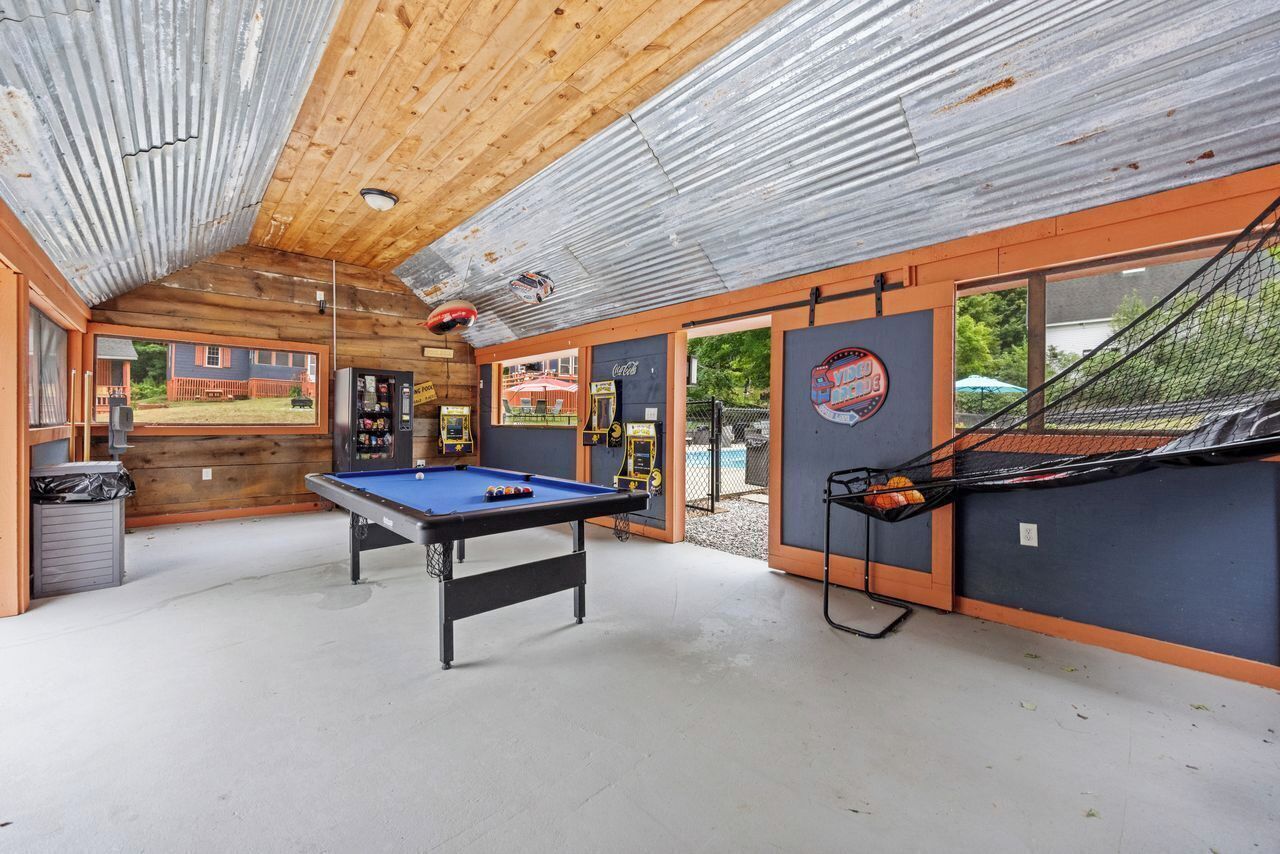 A pool table in a room with a wooden ceiling and a view of a house outside.