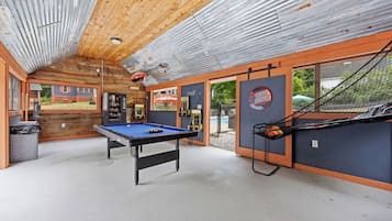 A pool table in a room with a wooden ceiling and a view of a house outside.