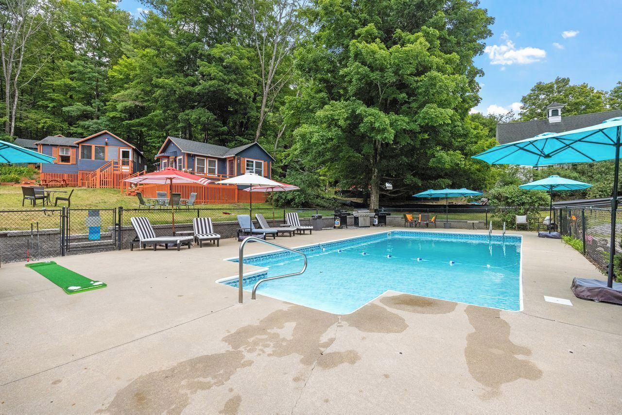 A swimming pool with lounge chairs and umbrellas, surrounded by a fence and trees.