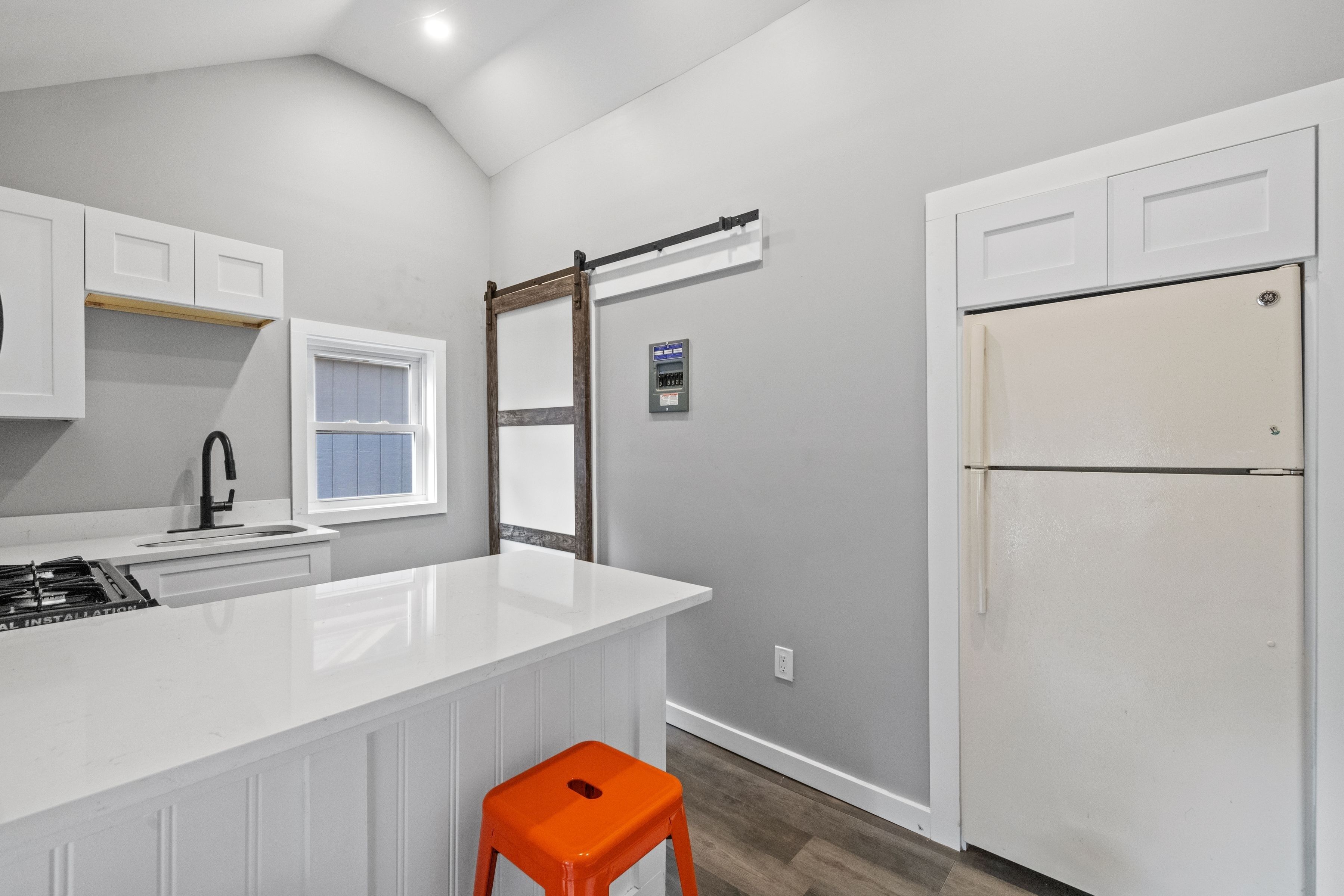 A kitchen with white cabinets, a white island, a window, a white refrigerator, and an orange stool.