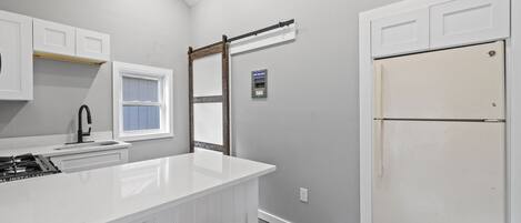 A kitchen with white cabinets, a white island, a window, a white refrigerator, and an orange stool.