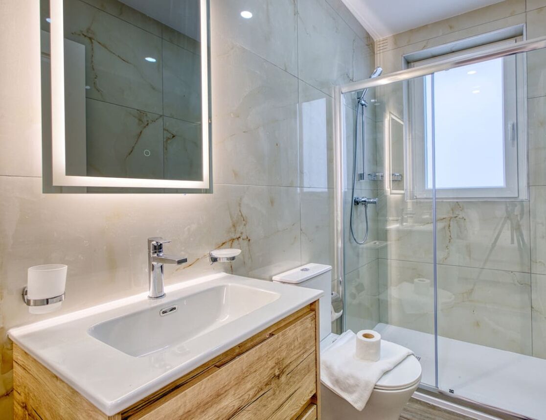 A modern bathroom with a large sink, mirror, and glass-enclosed shower.