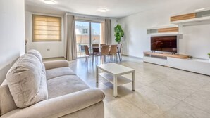 A modern living room with a sofa, a coffee table, a TV, and a dining area with chairs and a table. - Mellieha 3BR home with Rooftop Pool Access w/AC`s (Mellieħa)