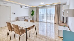 A modern living room with a marble table, beige sofa, and a large window with curtains.