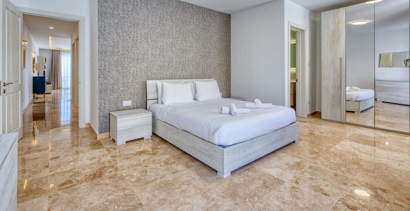 Ein modernes Hotelzimmer mit einem großen Bett, einem Nachttisch, einem Marmorboden und einem großen Spiegel.