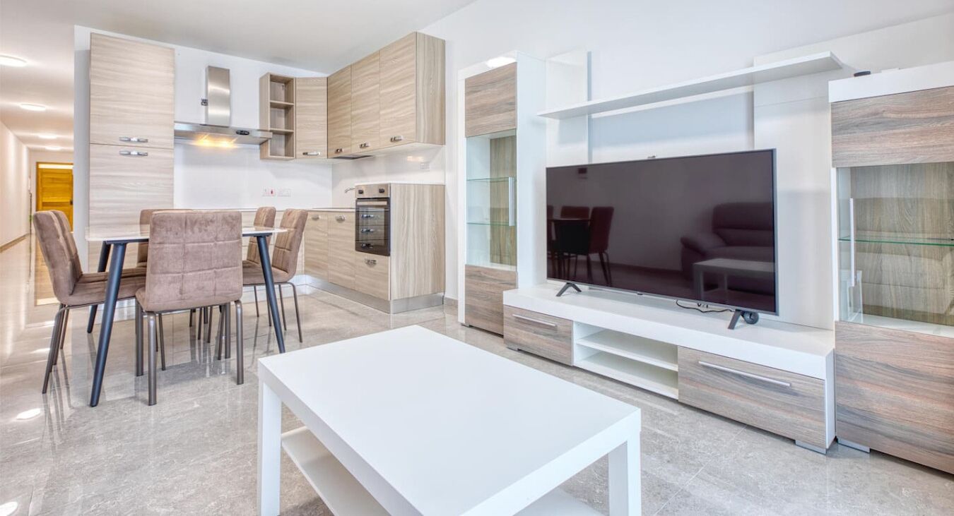 A modern living room with a flat-screen TV, a dining area with chairs, and built-in cabinetry.