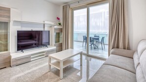 A modern living room with a flat-screen TV, a sofa, a coffee table, and a balcony with outdoor seating.
