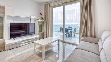 A modern living room with a flat-screen TV, a sofa, a coffee table, and a balcony with outdoor seating.