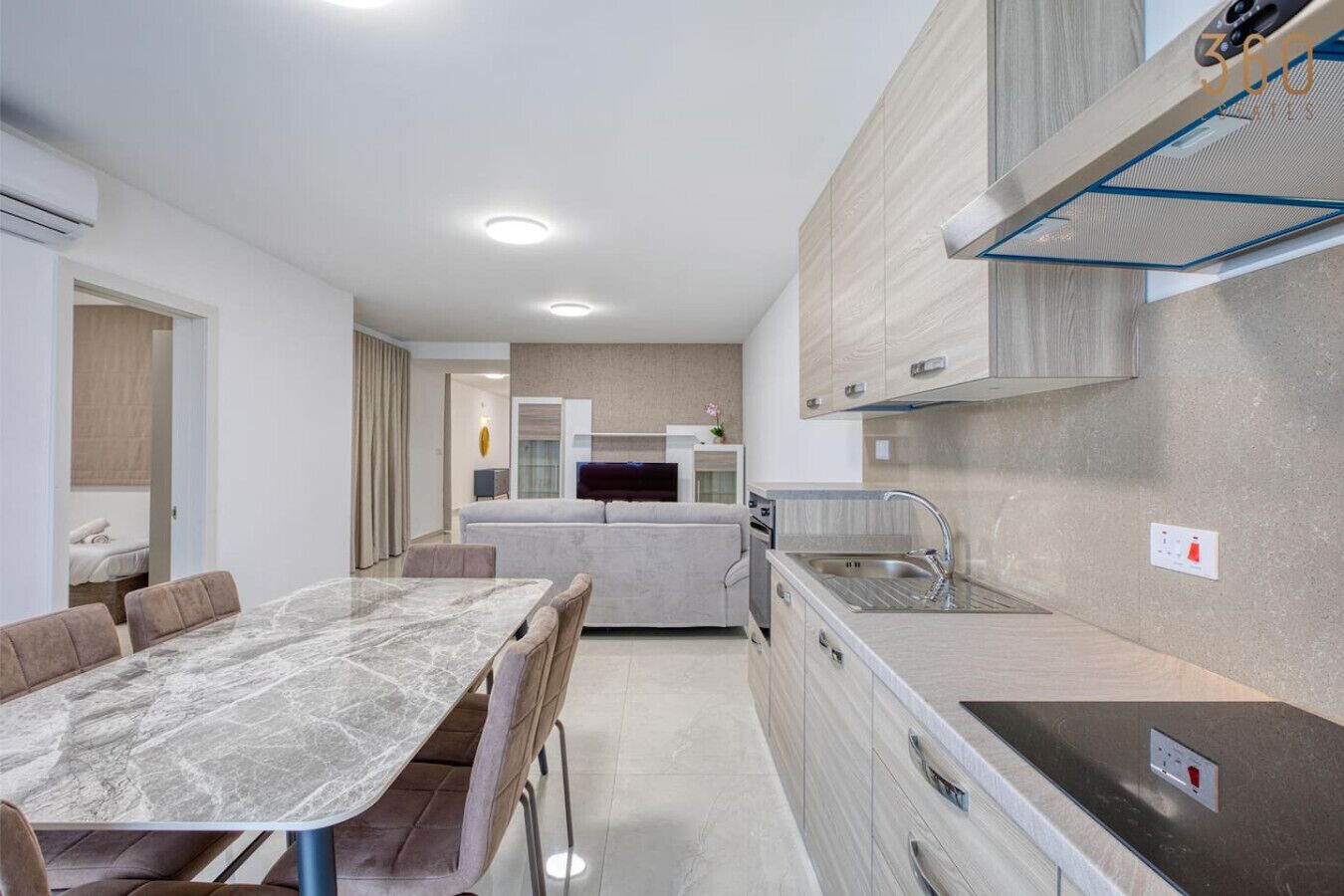A modern kitchen with a marble countertop, a built-in oven, and a sink.