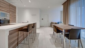 Une cuisine moderne dotée d’un îlot central, d’un coin repas avec une table et des chaises en bois, et d’une grande fenêtre agrémentée de rideaux.