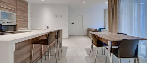 A modern kitchen with a central island, a dining area with a wooden table and chairs, and a large window with curtains.