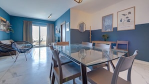 Un salón moderno con una mesa de comedor de cristal, paredes azules y vistas al exterior.