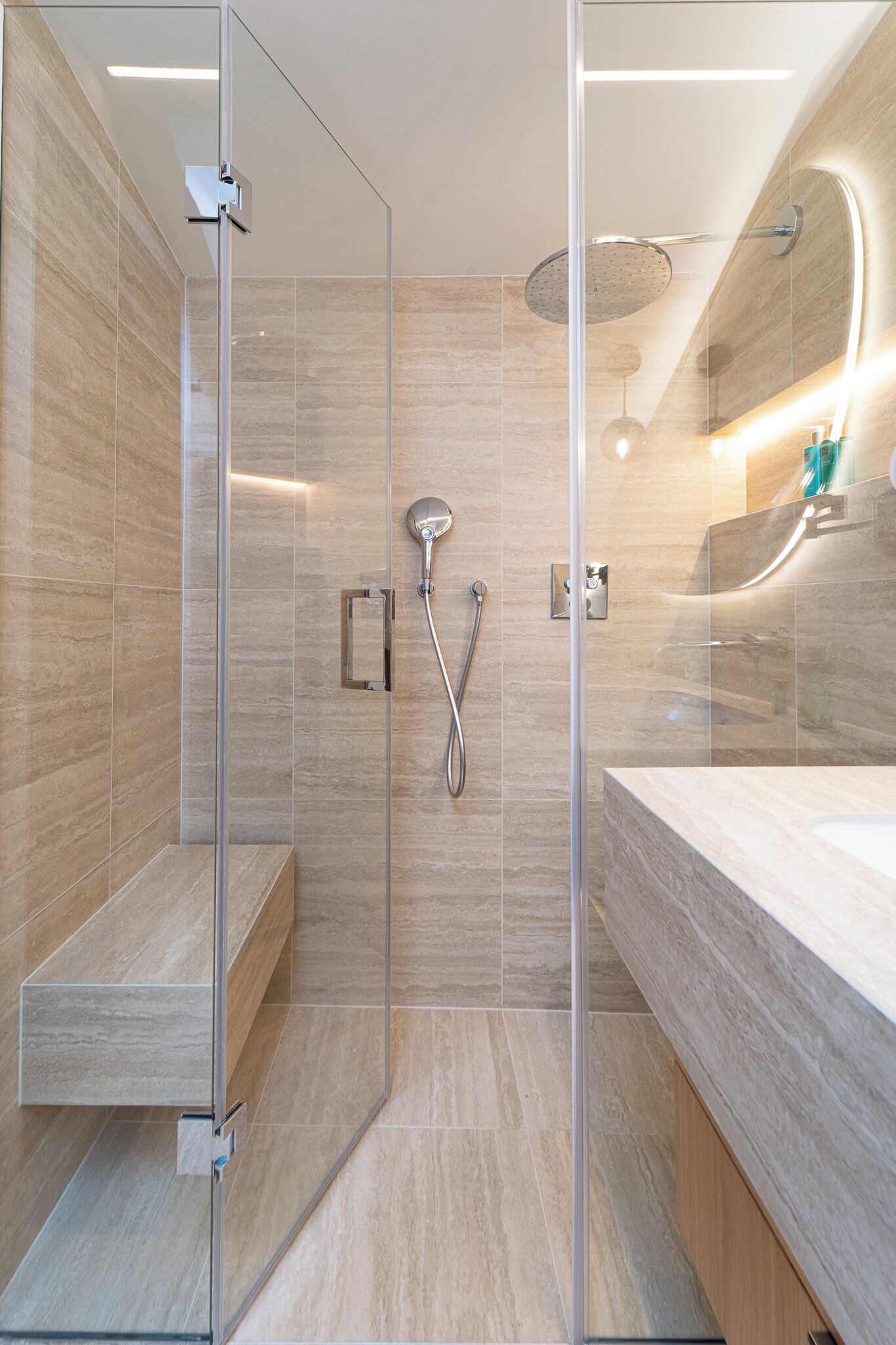 A modern bathroom with a glass-enclosed shower, a large mirror, and a marble-tiled vanity.